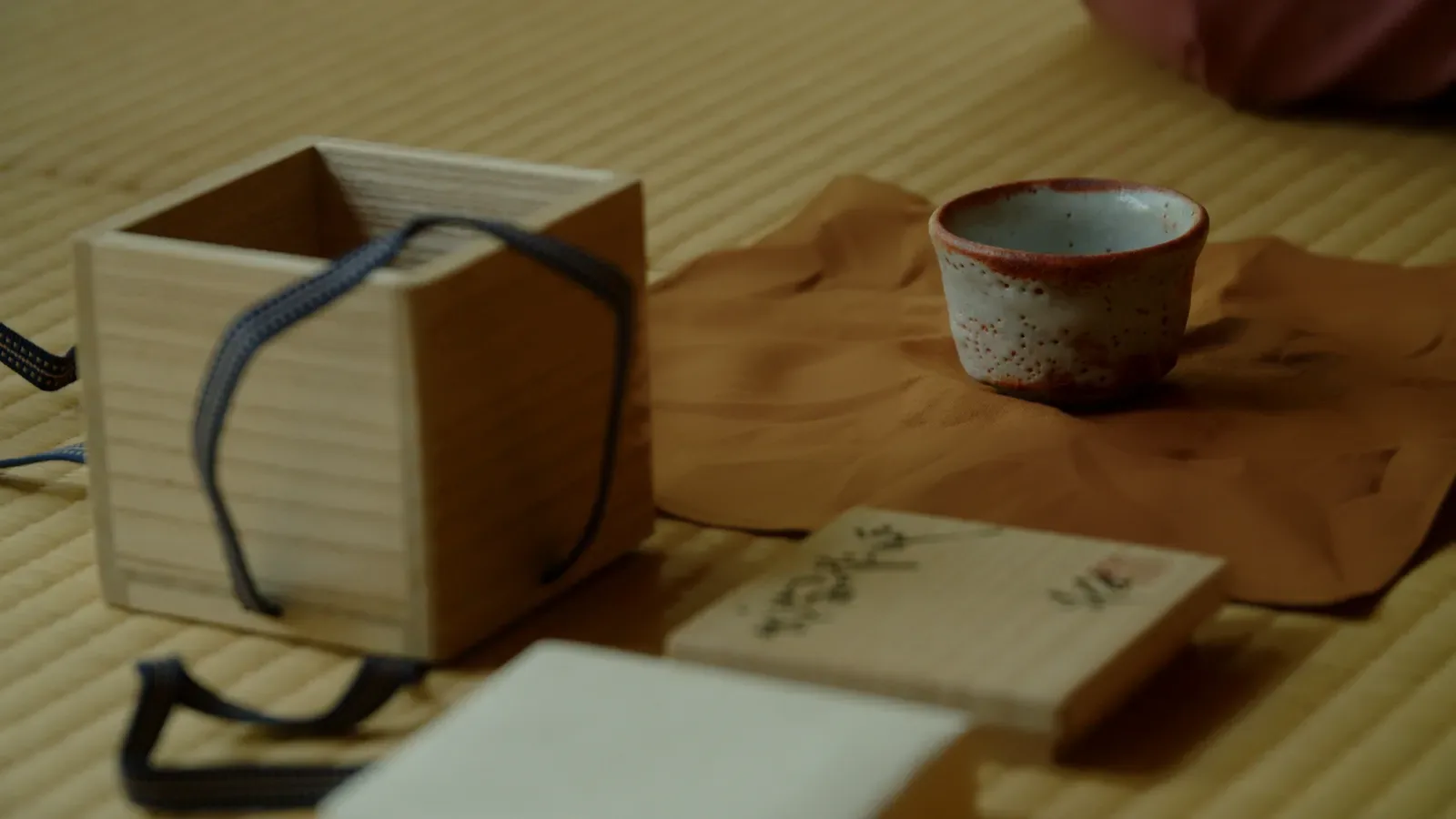 畳の上の桐箱と箱書きの蓋、布に置いた志野のぐい呑み